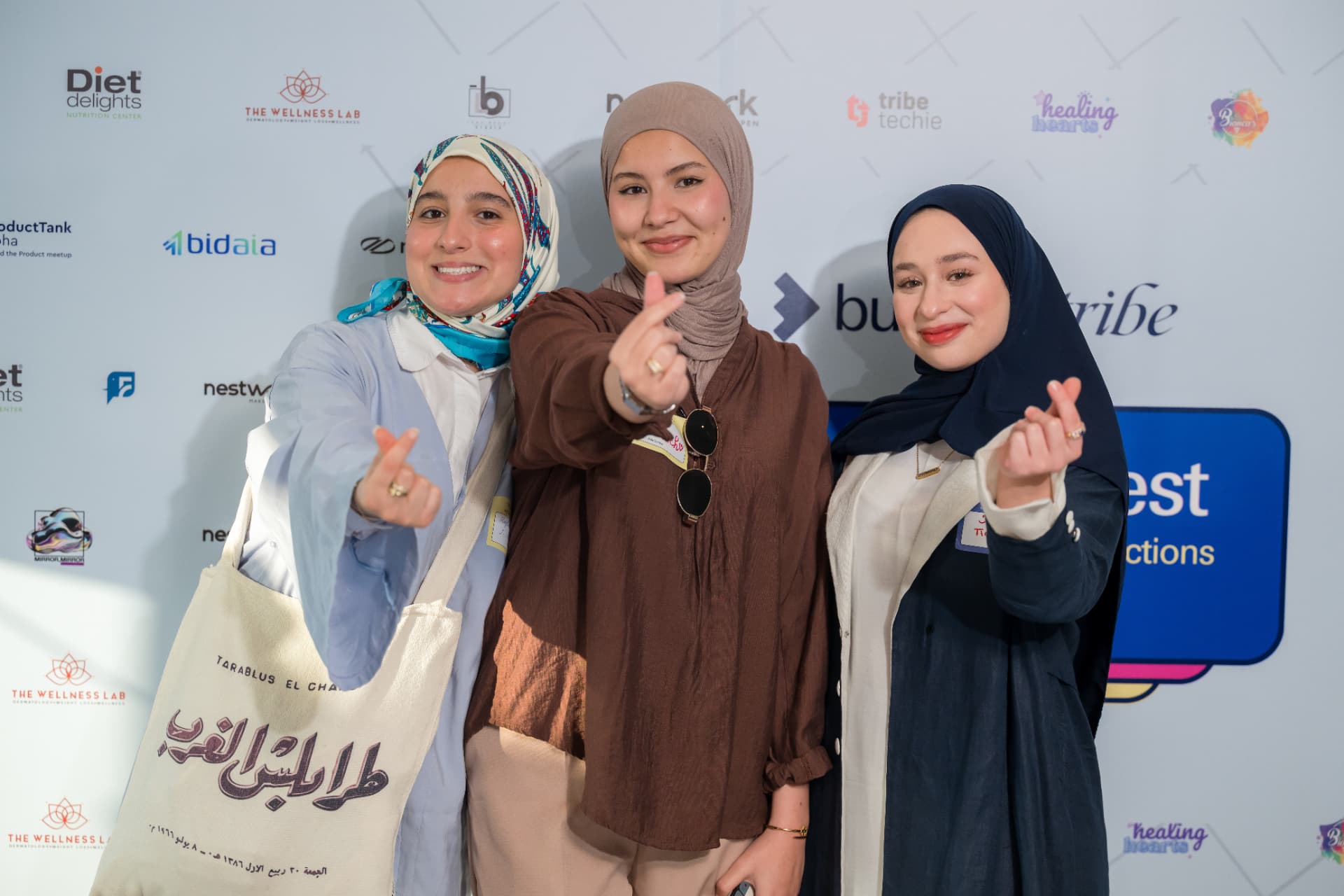 Three women posing together in front of sponsor logos