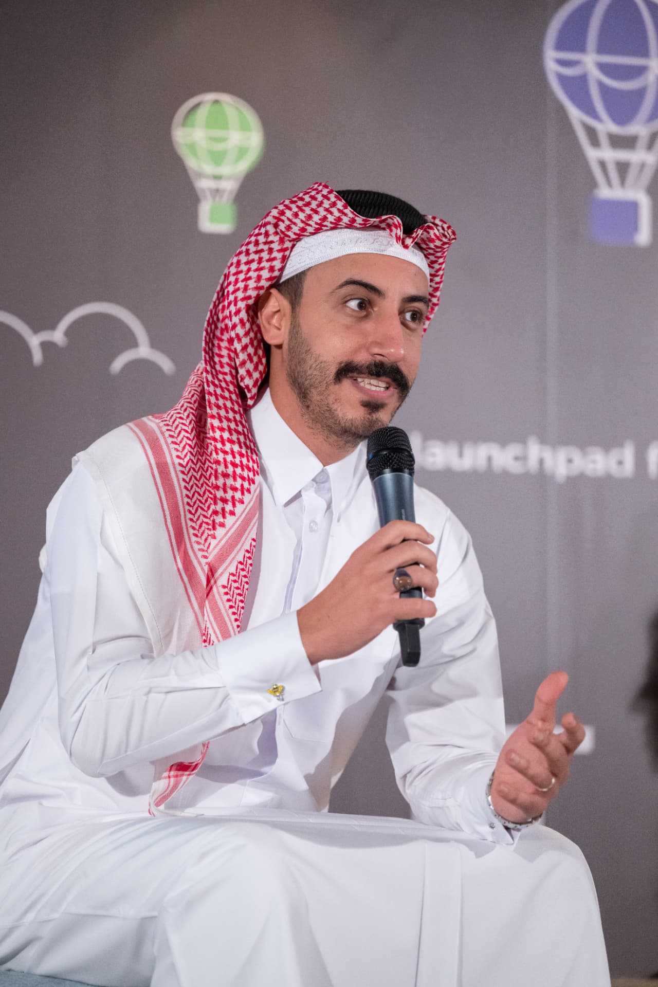 A seated speaker in traditional Qatari dress addressing the audience